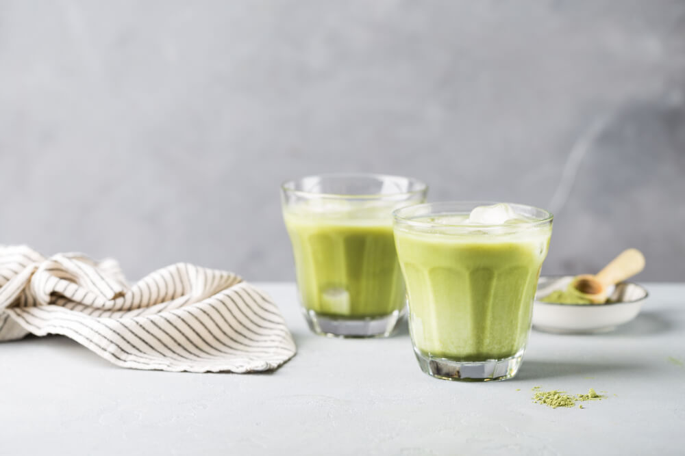 Matcha smoothie ve dvou sklenicích s ledem na šedém pozadí